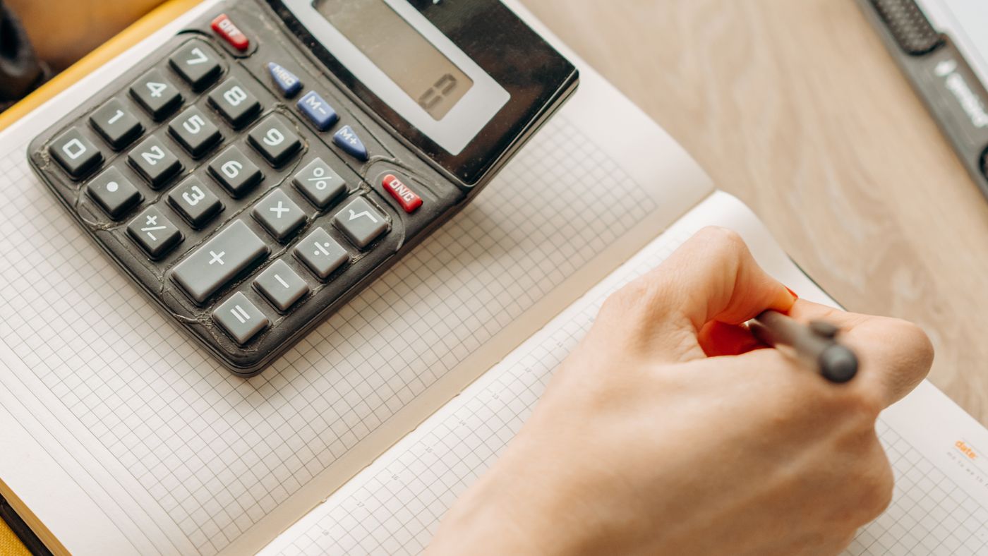 Hands preparing a written budget beside a calculator and paperwork