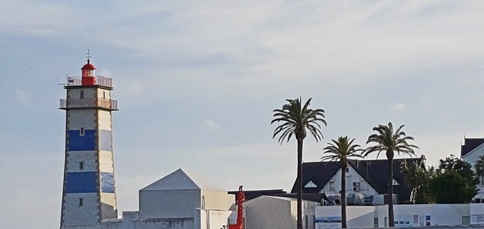 Santa Marta Lighthouse and coastal buildings beside palm trees in Cascais, Portugal